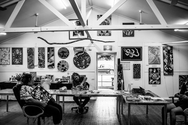 Black and white Coomaditchie art studio with Aboriginal artists working amid paintings on the walls