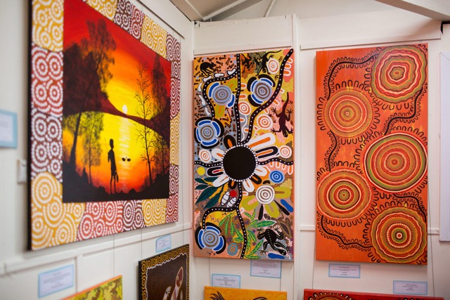 Coomaditchie gallery wall of bright Aboriginal paintings, including a sunset landscape and dot designs