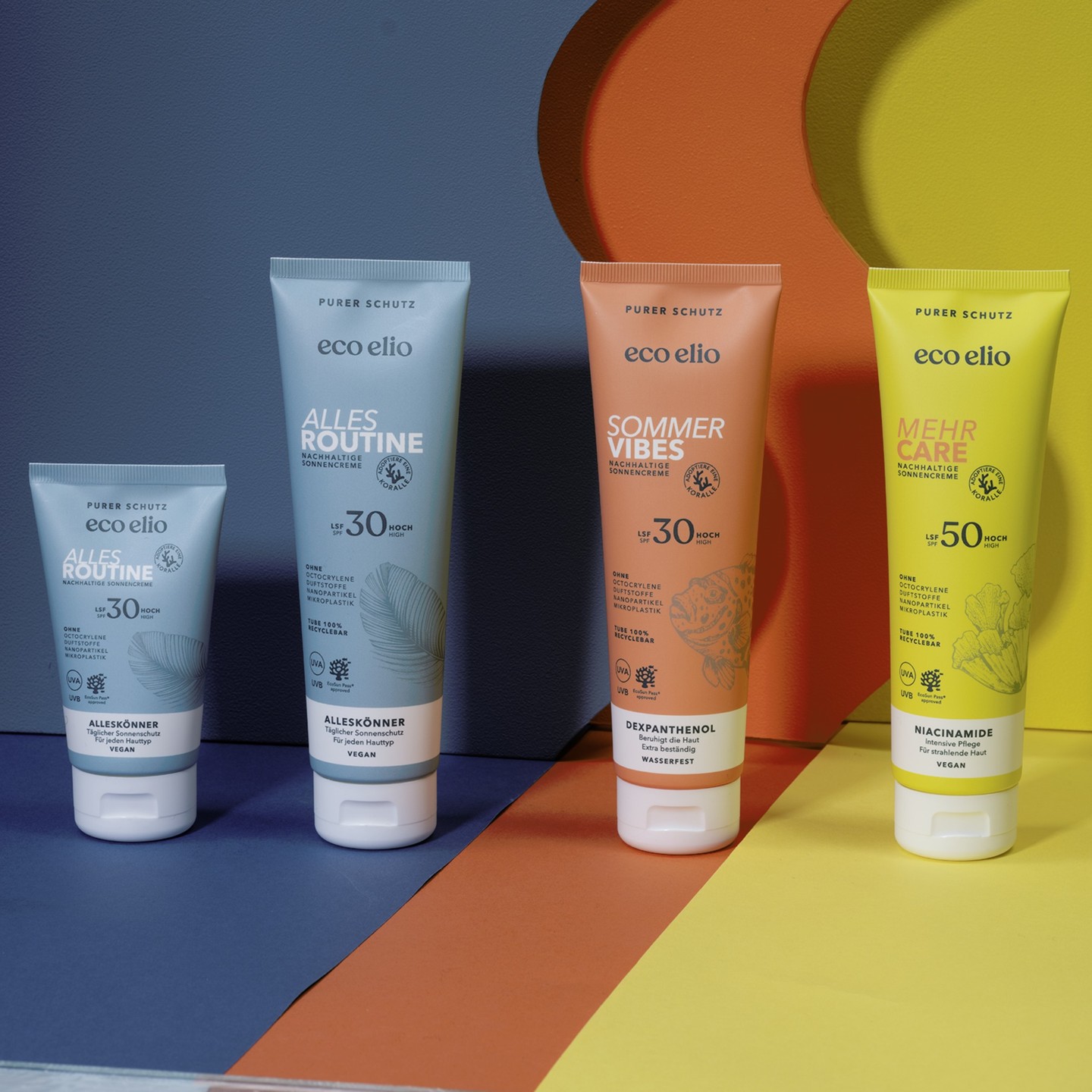 The eco elio sunscreen range of four tubes, including Sommer Vibes SPF30 and Mehr Care SPF50, on a colourful layered background